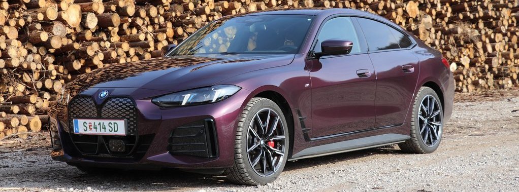 der neue BMW i4 40 xDrive Gran Coupé vor einem Holzhaufen