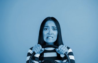 Young woman showing nervous expression with steering wheel on blue background